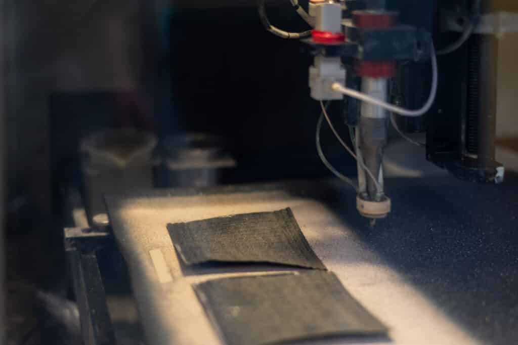 Close-up of an automated robotic dispenser applying a precision coating to flat substrates for catalyst and electrochemical component manufacturing.