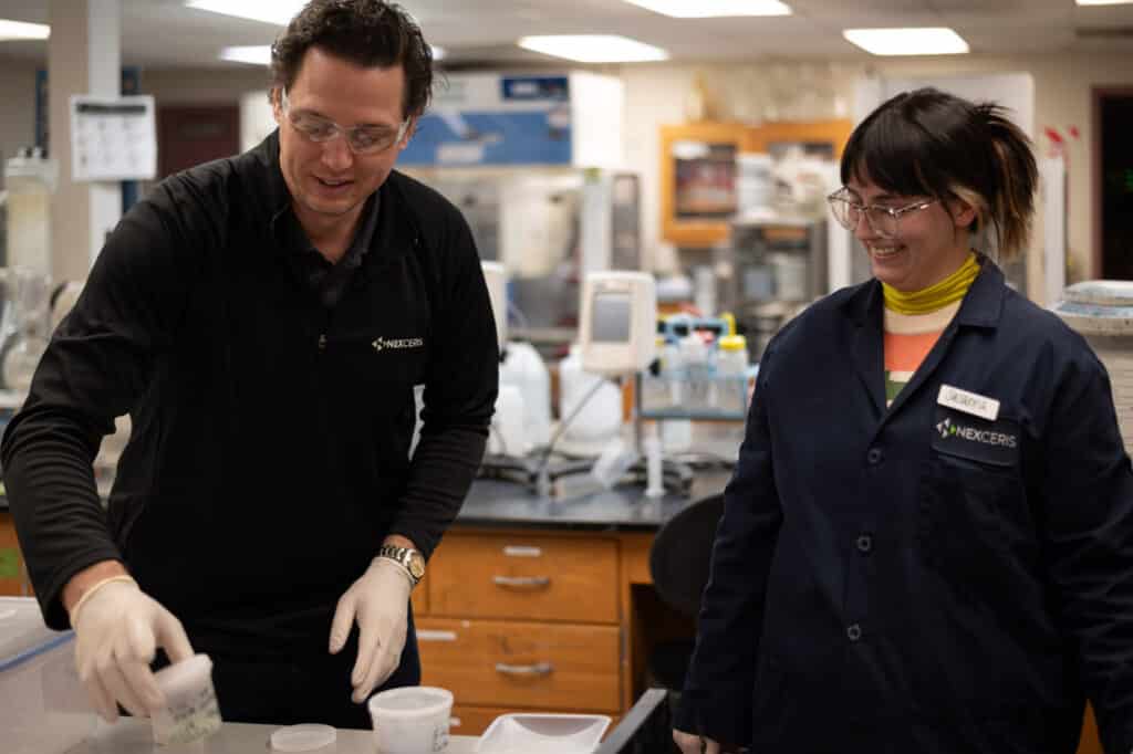 Two Nexceris research scientists happily collaborating on advanced material preparation in a chemical laboratory setting.