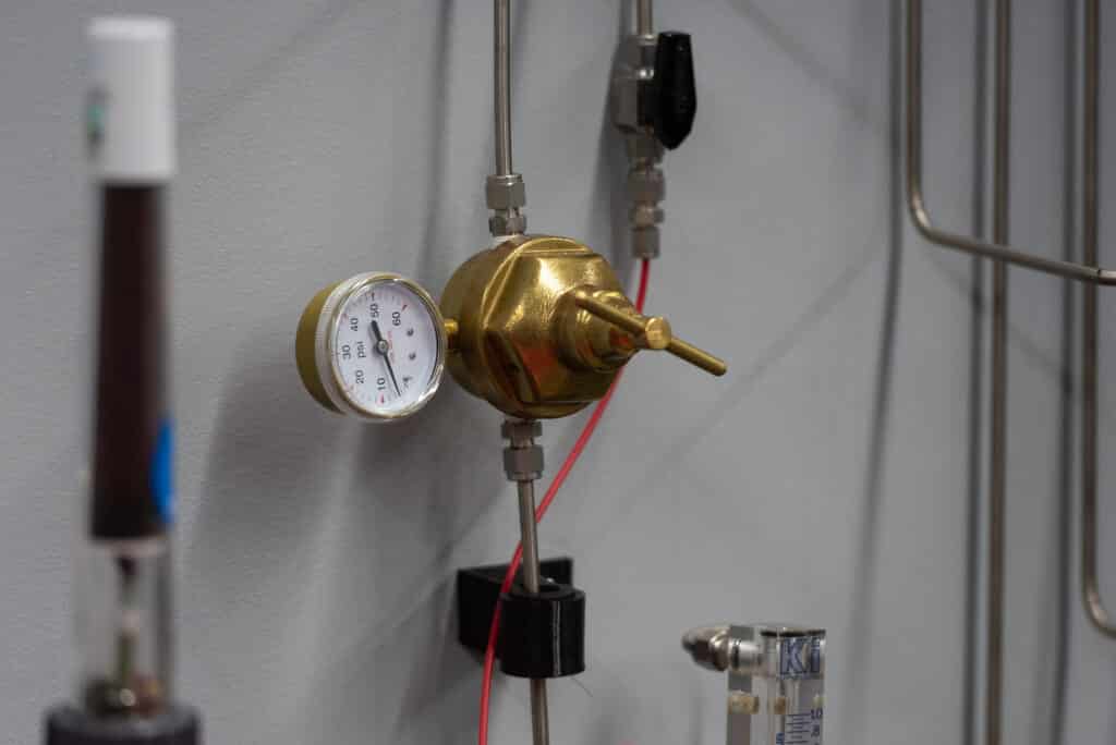 Close-up of a precision brass gas pressure regulator and gauge connected to stainless steel laboratory supply lines for advanced material testing.